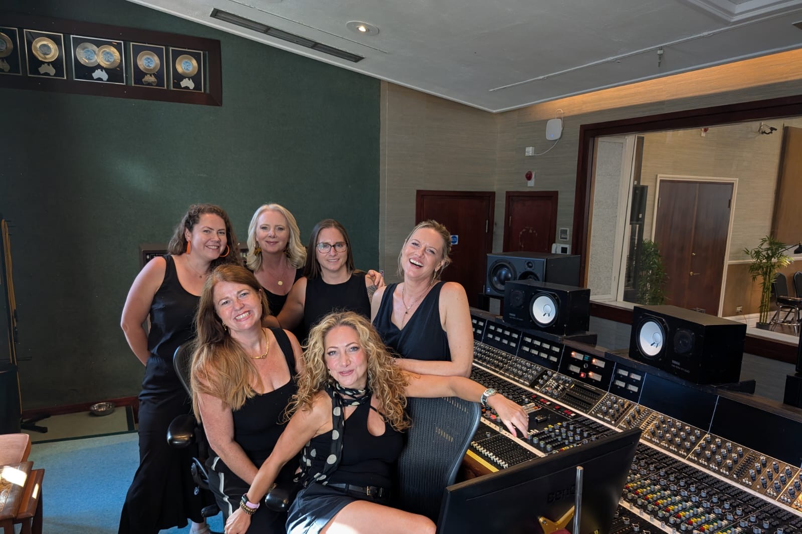 SLYMI members gathered around the mixing desk in a recording studio